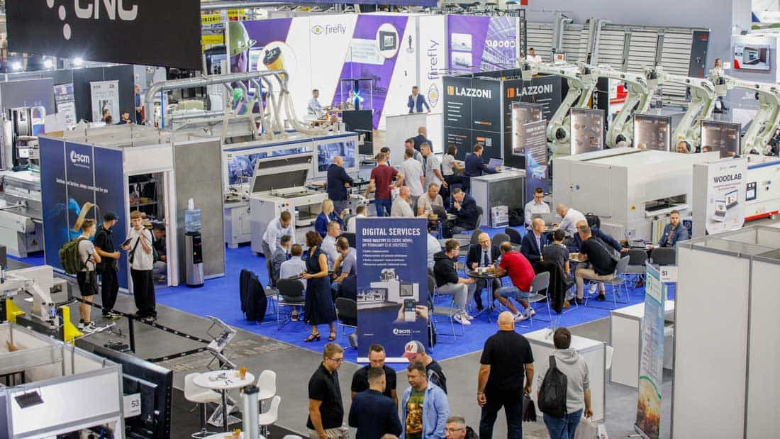 Fragment hali targowej DREMA 2025 z wystawcami prezentującymi innowacyjne technologie, robotykę i automatyzację dla przemysłu drzewnego i meblarskiego. Widoczne stoiska oraz goście.