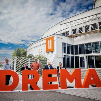 Uczestnicy targów DREMA 2025 pozują przy dużym napisie #DREMA przed halą Międzynarodowych Targów Poznańskich, symbolizującym wejście na wydarzenie.