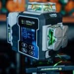 Niwelator laserowy STALCO 4D LLP4DG, zbliżenie na wyświetlacz i moduł emitujący zielone linie.