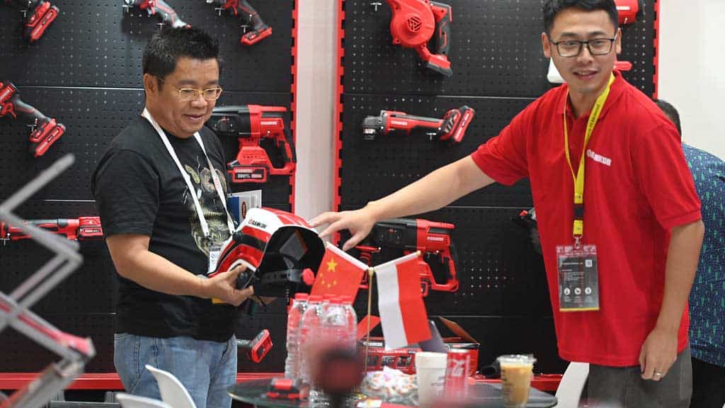 Kupiec ogląda maskę spawalniczą na stoisku z elektronarzędziami na targach International Hardware Fair Indonesia, w tle flagi Chin i Indonezji.