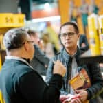 Uczestnik targów EISENWARENMESSE rozmawia z wystawcą przy stoisku z produktami budowlanymi/chemią w tubach.