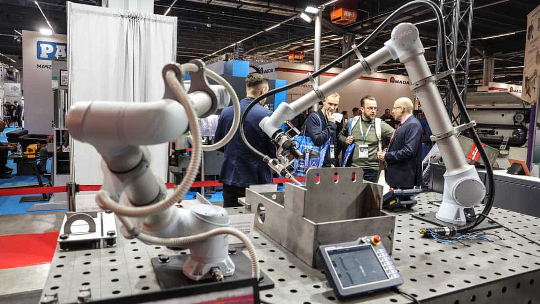 Prezentacja robota spawalniczego na stanowisku w hali targowej STOM. W tle widoczni zwiedzający i inżynierowie prowadzący rozmowy.