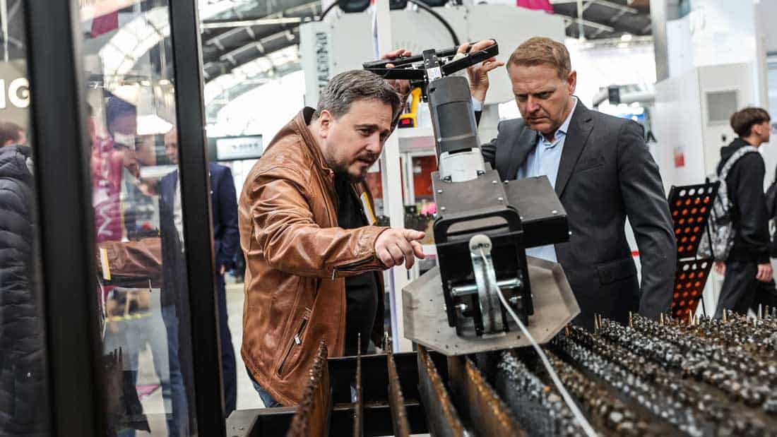 Eksperci oglądający maszynę do obróbki metalu na Targach Kielce. Uczestnik targów wskazuje na element robota tnącego lub spawającego.