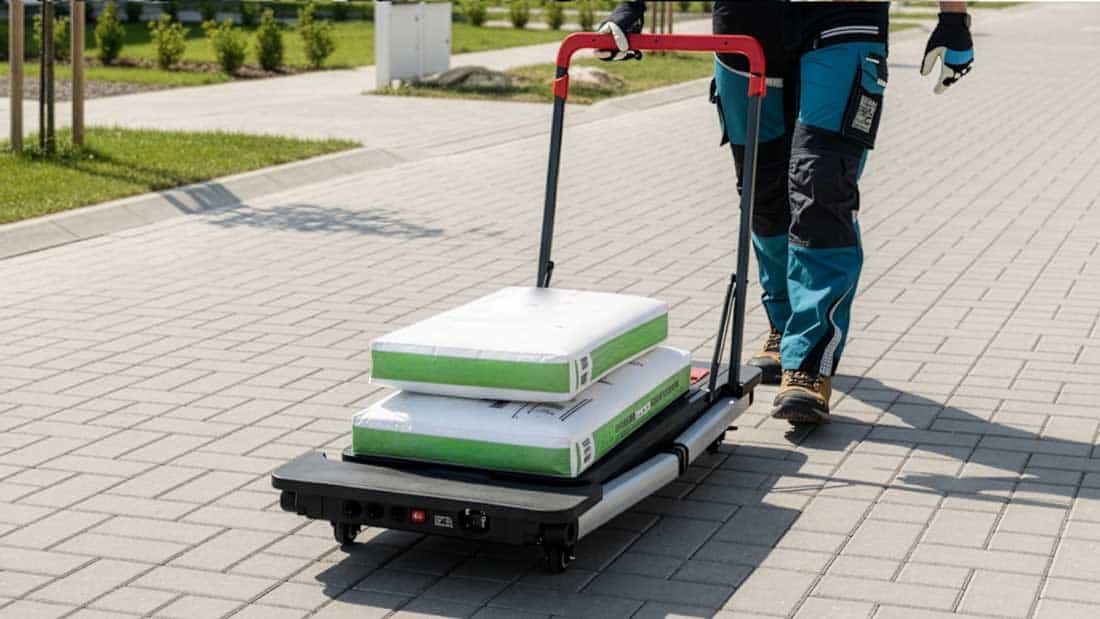 Osoba ciągnąca stół 62001 w konfiguracji wózka transportowego z workami materiałów na kostce brukowej.