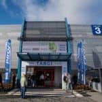 Wejście do Hali 3 Targów Kielce z banerem Targów Ogród i Dekoracje Grupy PSB. Przed wejściem widoczne niebieskie flagi reklamowe PROFI oraz kilku uczestników.