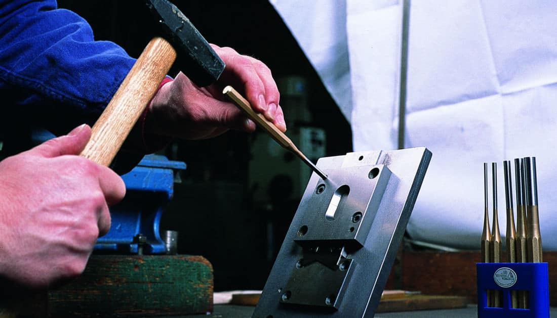 Użycie wybijaka klasycznego Rennsteig (złocony) z młotkiem do pracy precyzyjnej na elemencie metalowym, w tle widoczny zestaw punktaków.