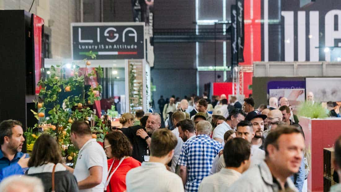 Stoisko LISA Luxury is an Attitude na targach spoga+gafa, wokół którego gromadzą się tłumy odwiedzających. Widoczne elementy dekoracyjne, w tym doniczkowe drzewko. (Stoisko wystawowe, meble ogrodowe, luxury outdoor, tłum, garden lifestyle)