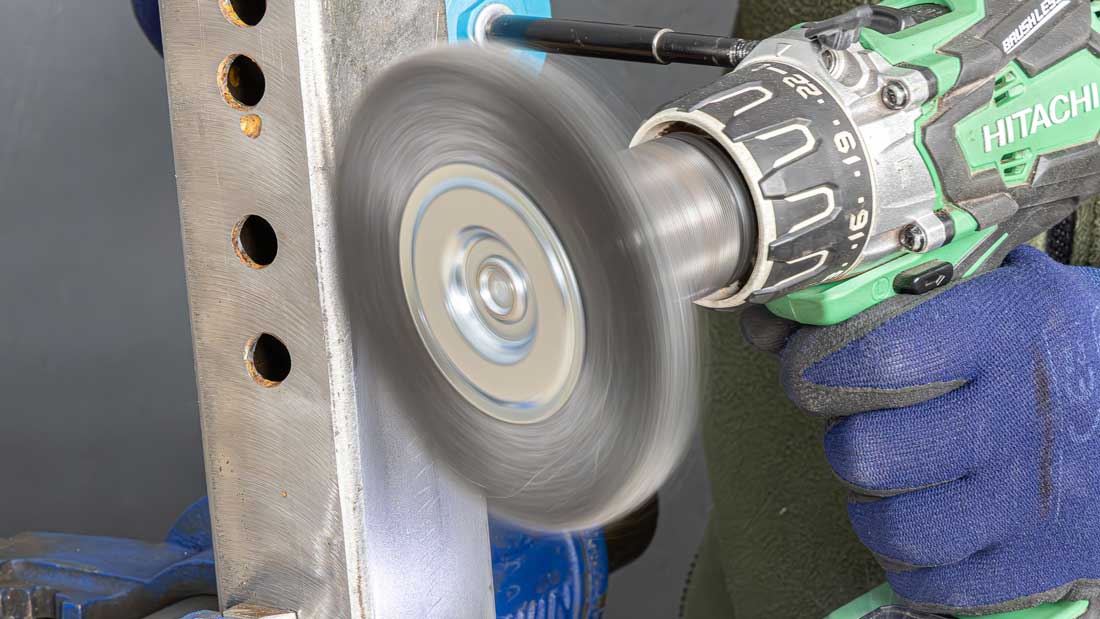 Szczotka techniczna na trzpieniu Klingspor usuwająca zabrudzenia z profilu stalowego z otworami przy użyciu wiertarko-wkrętarki.