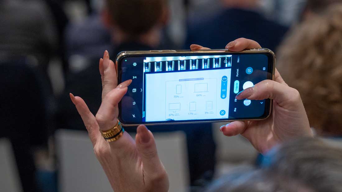 Zbliżenie na dłonie uczestniczki robiącej zdjęcie smartfonem slajdu prezentacji podczas konferencji