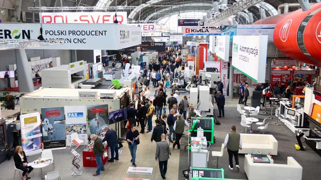 Widok ogólny na halę wystawienniczą Targów Kielce podczas Przemysłowej Wiosny. Widoczne liczne stoiska z maszynami CNC (m.in. Pol-Sver, Kimla), banery reklamowe oraz tłum zwiedzających spacerujących alejkami targowymi.