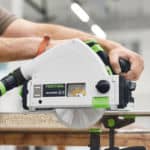 Akumulatorowa pilarka zagłębiarka Festool TSC 55 KS podczas cięcia płyty drewnopochodnej z użyciem szyny prowadzącej i odsysania pyłu