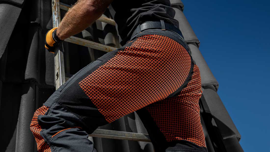 Dekarz podczas pracy na dachu, ubrany w spodnie robocze LAHTI PRO, w trakcie wejścia po drabinie na stromą połać dachową