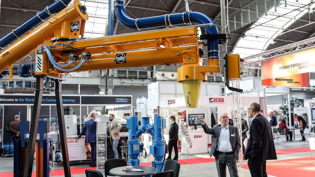 Stoisko targowe z systemem transportu i dozowania materiałów sypkich dla odlewnictwa podczas targów przemysłowych w Targach Kielce; widoczne instalacje filtrowentylacyjne oraz rozmowy biznesowe przedstawicieli branży.