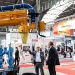 Instalacja transportu i odpylania materiałów w hali targowej podczas wydarzenia przemysłowego w Targach Kielce; widoczne stoisko technologii dla odlewnictwa oraz rozmowy przedstawicieli branży metalurgicznej.