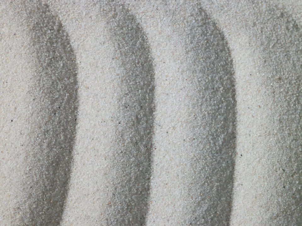 Zbliżenie na drobnoziarnisty piasek kwarcowy o jasnej barwie z widocznymi smugami po przesunięciu materiału