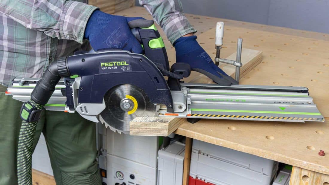 Akumulatorowa pilarka tarczowa Festool HKC 55 KEB podczas precyzyjnego cięcia drewna na prowadnicy FSK w warsztacie stolarskim.