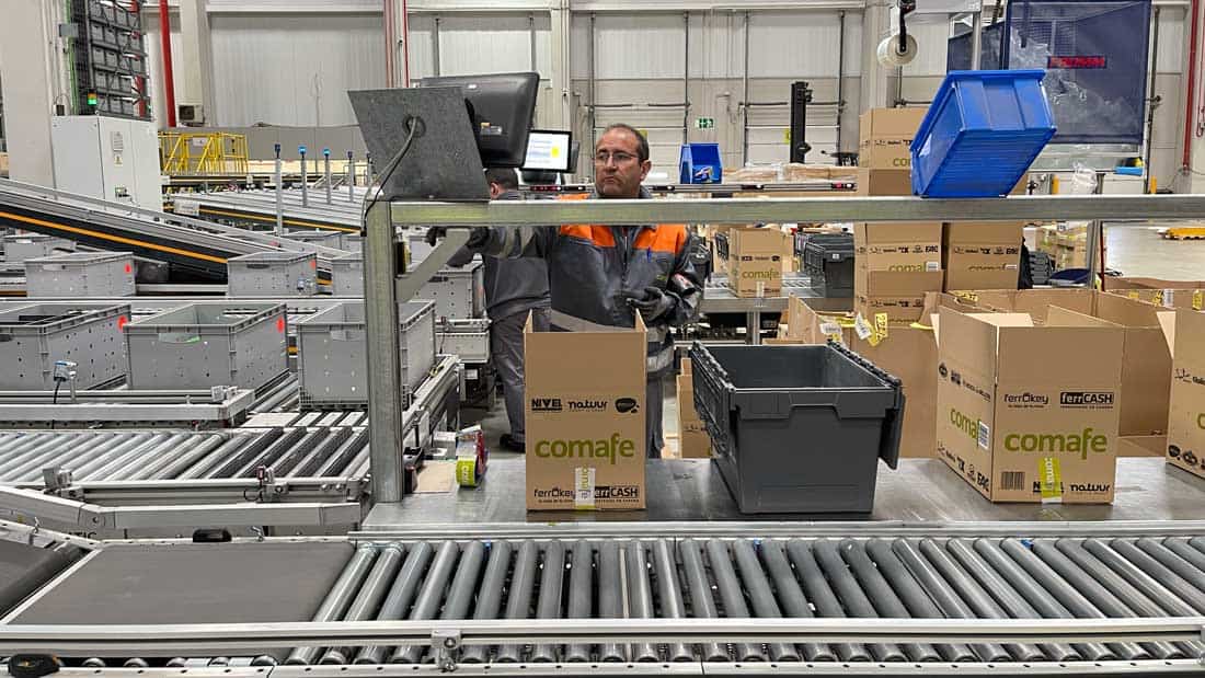 Pracownik kompletujący zamówienia w zautomatyzowanym centrum logistycznym branży DIY z liniami transportowymi i systemem sortowania paczek.