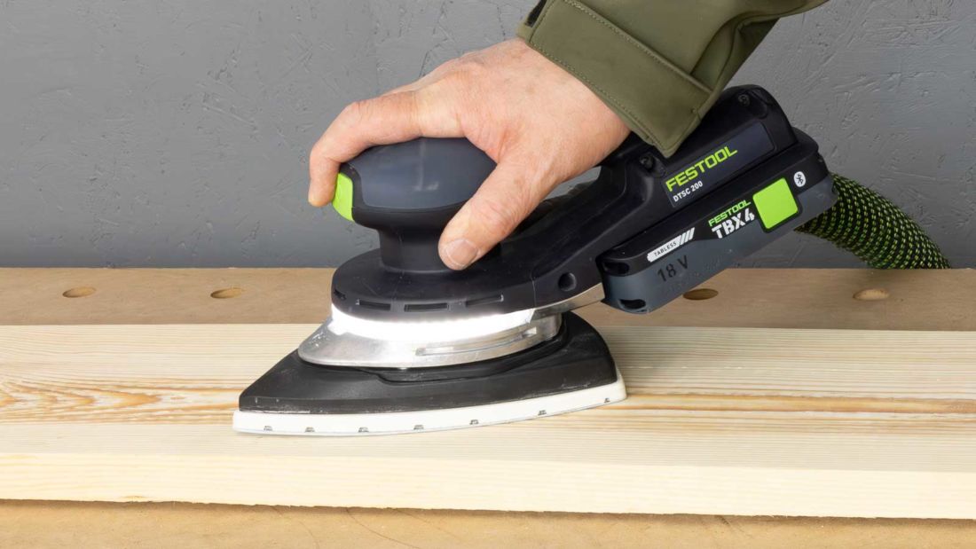 Akumulatorowa szlifierka delta Festool DTSC 200 podczas szlifowania deski drewnianej, pierścień LED doświetlający powierzchnię