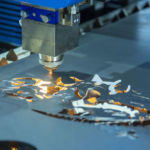 Precyzyjne cięcie blachy stalowej laserem fiber – głowica wycinarki podczas pracy, widoczne iskry i detale wycinanych elementów metalowych