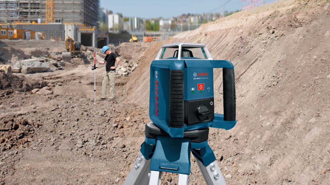 Niwelator laserowy Bosch Professional ustawiony na statywie podczas pomiarów na dużym placu budowy.