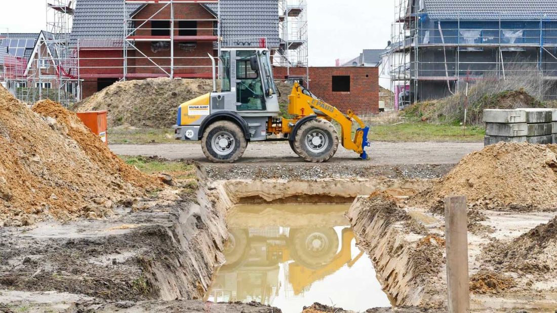Plac budowy z zalanym wykopem fundamentowym i maszyną budowlaną pracującą przy odwodnieniu terenu